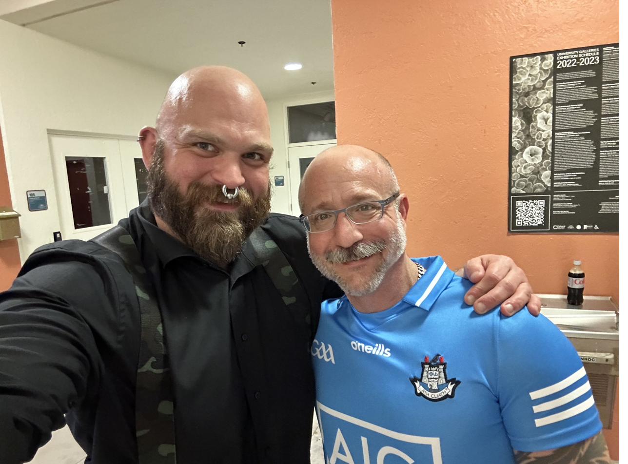 Barclay Barrios smiling, standing with a friend in an embrace.